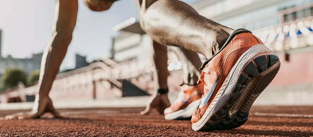 A runner wearing orange shoes on a track with a blurred background, suggesting motion.