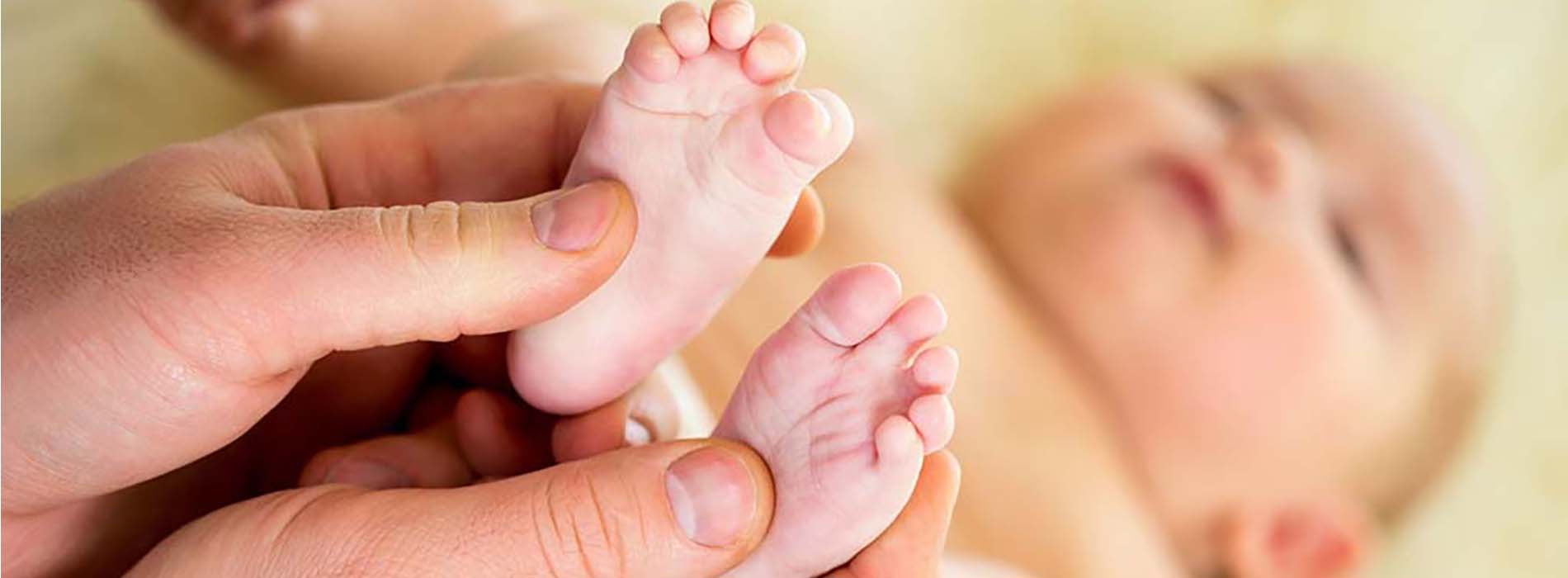 A hand holding two tiny feet with toes visible against a soft, light background.