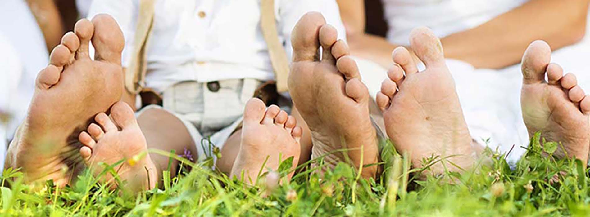 The image shows four feet resting on grass with a blurred background featuring two people sitting close together.