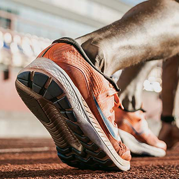 A person s feet wearing orange and blue running shoes are captured mid-stride on a track, with the focus on the soles of the shoes.